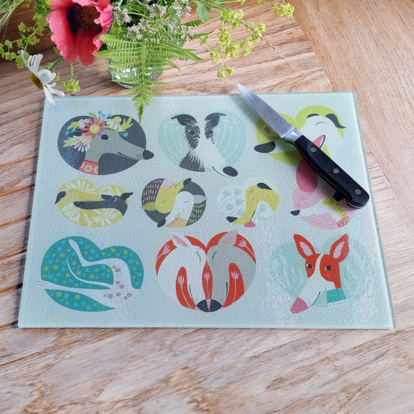 A Noses & Poses glass chopping board, shown from above on an oak worktop, with a paring knife, next to fresh flowers