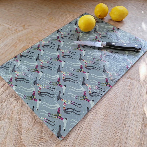 A glass chopping board with the Sleepy Sighthounds pattern, shown flat on an oak worktop, alongside lemons and a small knife