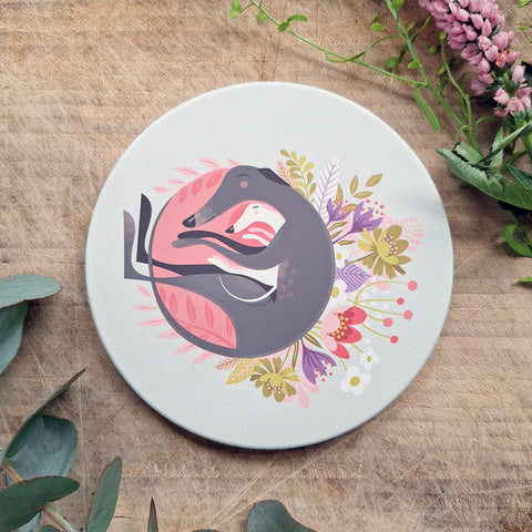 A matt ceramic coaster featuring the Spring Snuggling illustration, two hounds hugging on a bed of Spring flowers. flowers and eucalyptus springs surround the coaster.