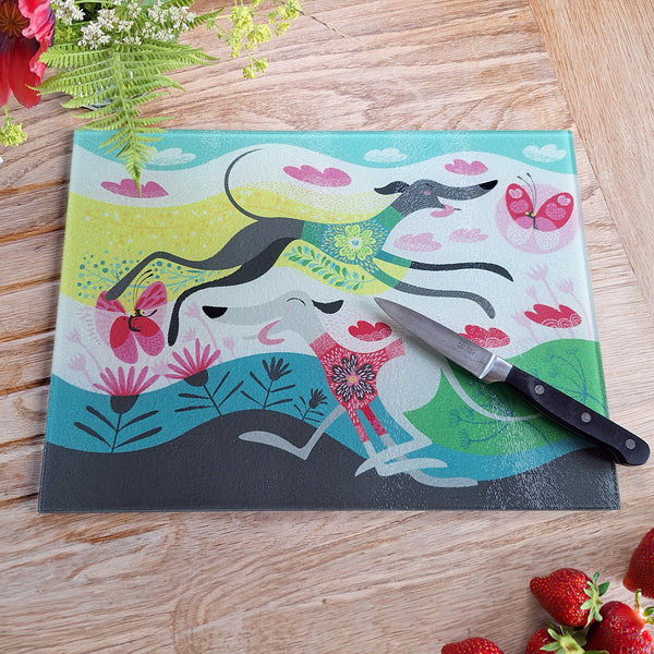 A zoomies glass chopping board, photogrpahed from above on an oak work surface,  next to fresh flowers and strawberries