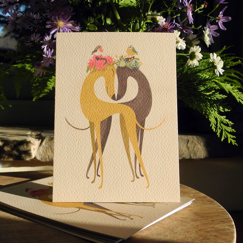 Hounds of Love postcards by Rolelrdog, shown on a table with a bunch of flowers in the background