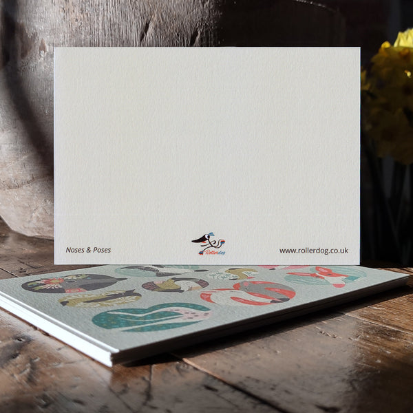 The back of a Noses & Poses postcard shown on a stack of the cards