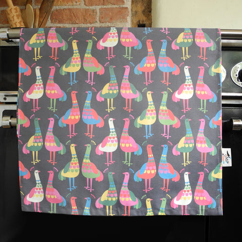 A Haughty Peacocks tea towel by Rollerdog, shown hanging on an oven door