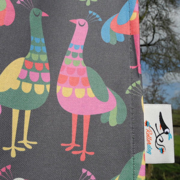 A close up view of a Haughty Peacocks tea towel by Rollerdog, showing the fabric weave and the Rollerdog label
