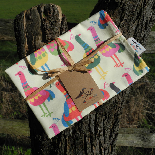A Haughty Peacocks tea towel shown folded and wrapped in raffia complete with a Rollerdog tag