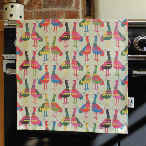 A Haughty Peacocks tea towel by Rollerdog, hanging on an oven door inside a kitchen