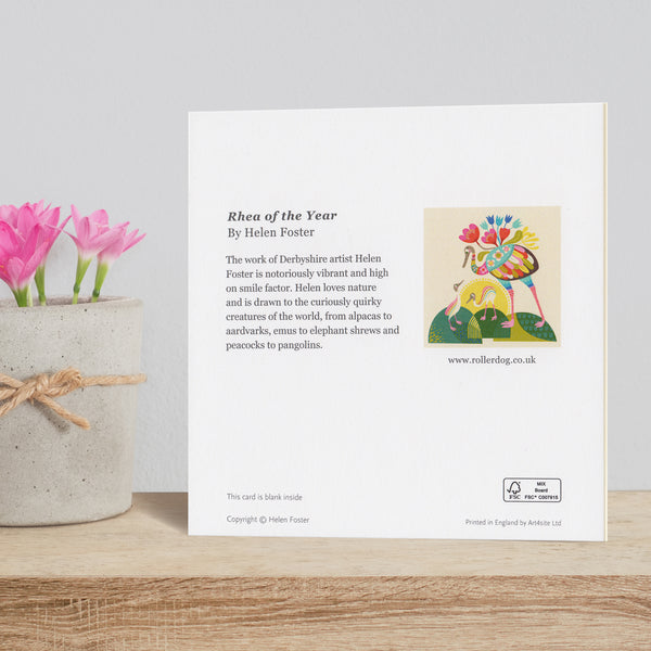 Rear view of a Rhea of the Year card by Rollerdog, shown on a shelf next to a pot of crocus