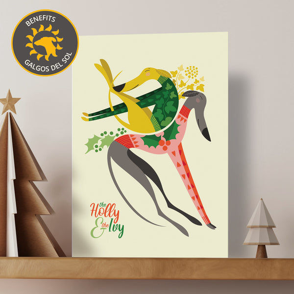 A Christmas card featuring two illustrated sighthounds in festive jumpers. The card sits on a wooden shelf