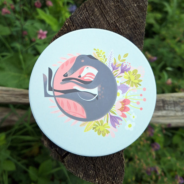A 'Spring Snuggling' ceramic coaster photographed on a wooden post in the countryside