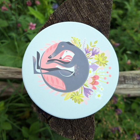 A 'Spring Snuggling' ceramic coaster photographed on a wooden post in the countryside