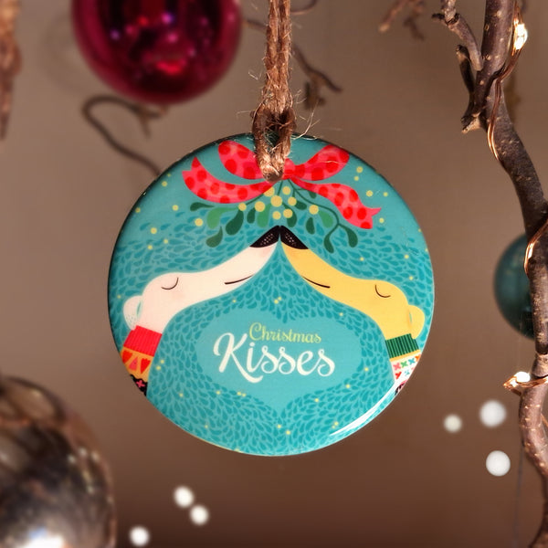 A flat ceramic disk decorated with artwork called Christmas Kisses, two hounds snout to snout under mistletoe