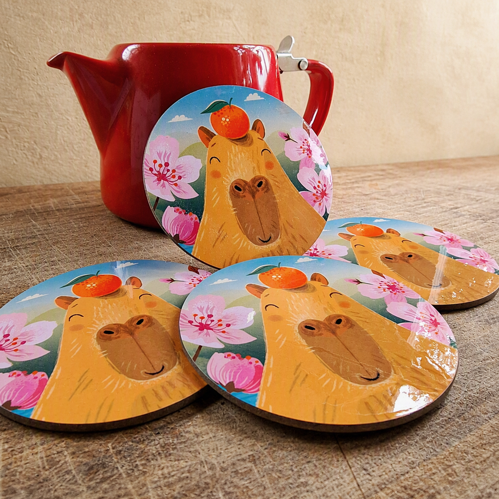 A set of 4 coasters featuring a capybara illustration, on a wooden surface, leaning against a red teapot