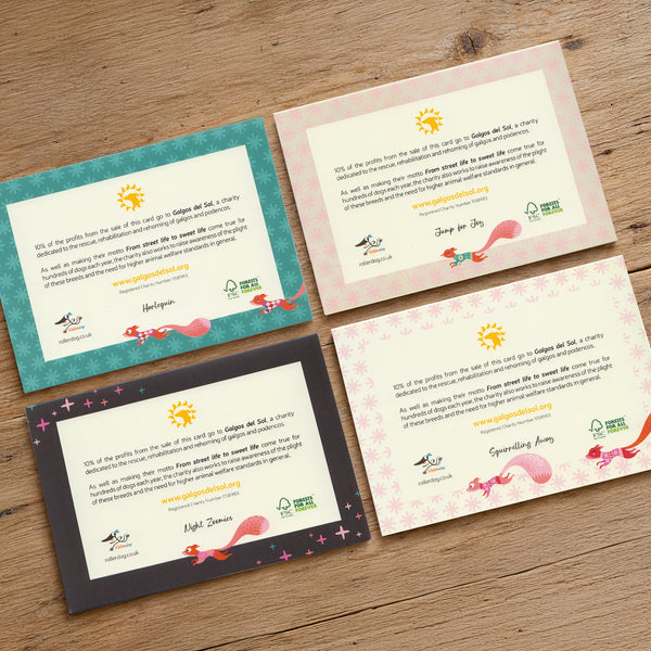 The back of the 4 Rollerdog 2026 Christmas cards, showing the written information about 10% off the profits going to the charity Galgos del SOl. The cards are laid facing down on a rustic wooden surface.