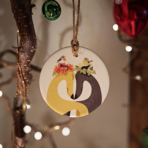 A ceramic decoration with Rollerdog's Hounds of Love illustration, shown hanging from a twiggy Christmas tree with twinkly fairy lights