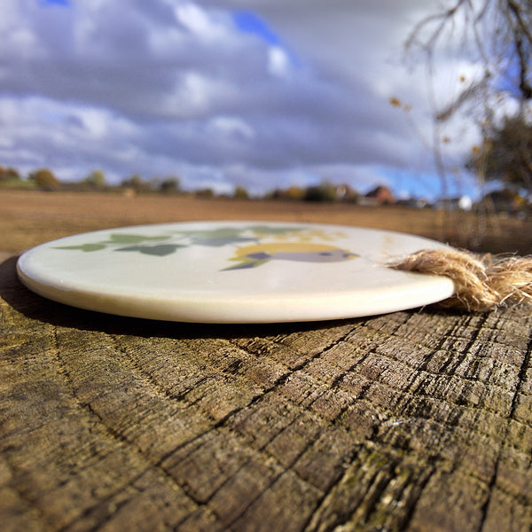 SIde view of a ceramic decoration by Rollerdog, showing the thickness of the disk and twine hanger