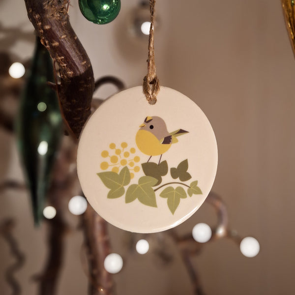 A ceramic decoration featuring a goldcrest bird, hanging on a twiggy Christmas tree with fairy lights