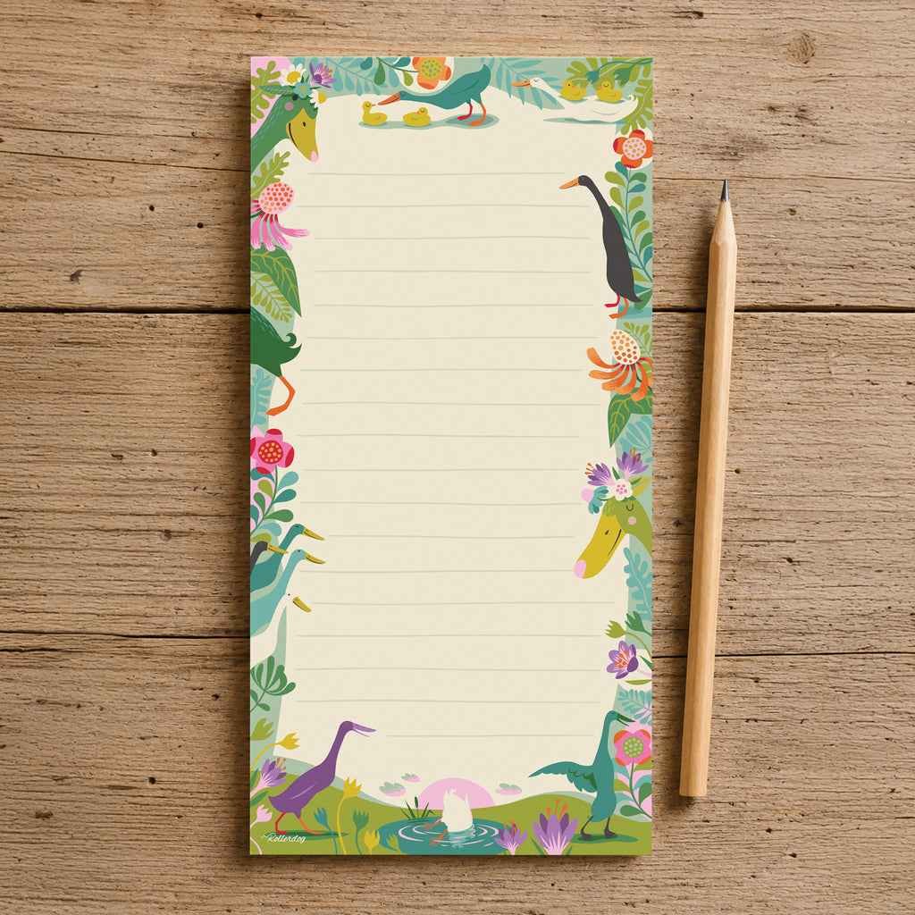 A lined notepad with a colourful illustrated border of Indian runner ducks, flowers and foliage, placed on a rustic wooden surface next to a wooden pencil.