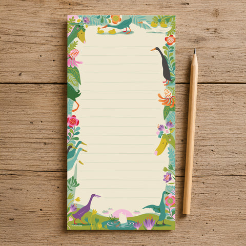A lined notepad with a colourful illustrated border of Indian runner ducks, flowers and foliage, placed on a rustic wooden surface next to a wooden pencil.