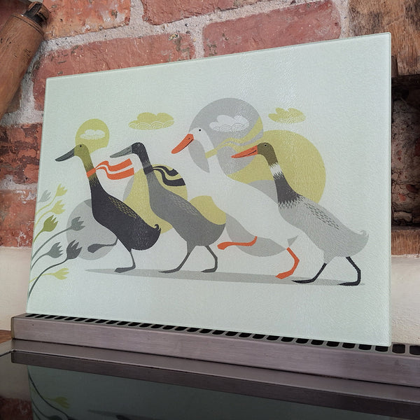 A Derbyshire Ducks glass chopping board leaning against a birck wall on top of an oven hob