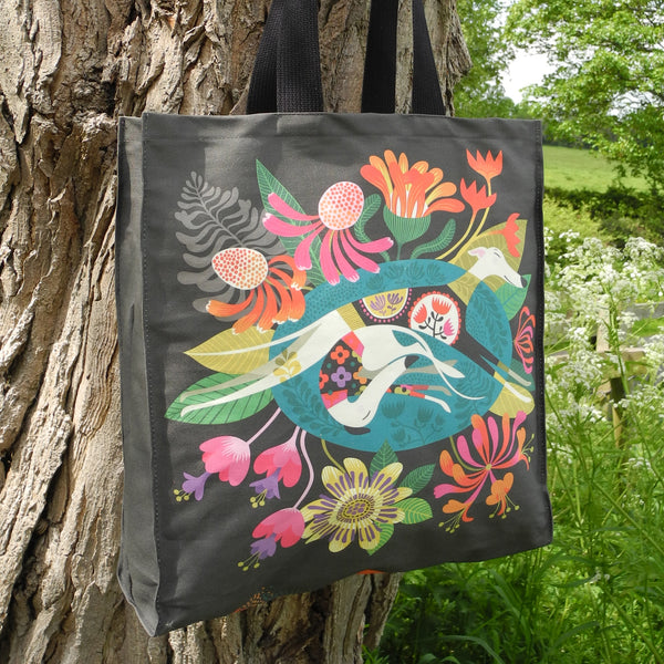 A Flowerbed tote bag by Rollerdog, photographed against a tree in the countryside