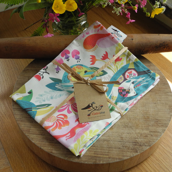 A folded Flowerbed tea towel, shown on a bamboo chopping board, over an old rolling pin