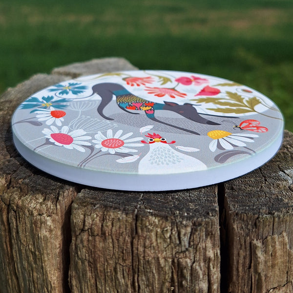 A Greta Greyhound ceramic coaster photographed outside on a wooden post, showing the thickness of the coaster