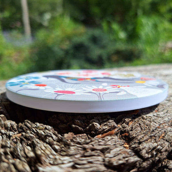 A Greta Greyhound ceramic coaster photographed outside on a wooden surface, showing the thickness of the coaster