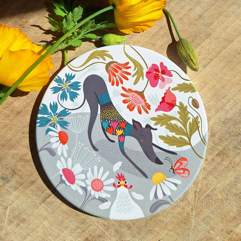 A Greta Greyhound ceramic coaster set on a wooden worktop with yellow poppies