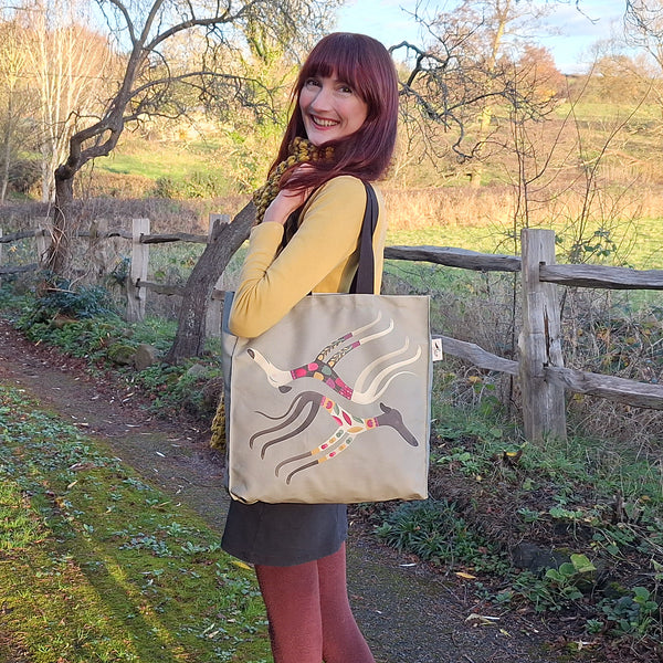 A Sleepy Sighthounds tote bag being shown in use, being  worn as a shoulder bag in a countryside setting