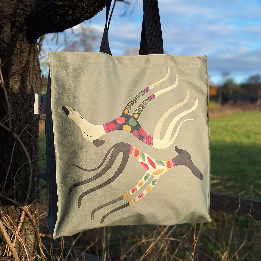 A Rollerdog tote bag with the Sleepy Sighthounds design, shown in a countryside setting