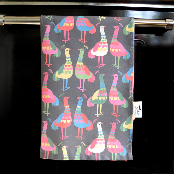 A Haughty Peacocks tea towel by Rollerdog, shown hanging on an oven door