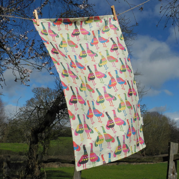 A Haughty Peacocks tea towel by Rollerdog, shown pegged on a washing line in the countryside