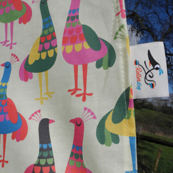 A close up view of a Haughty Peacocks tea towel, showing the weave of the fabric and the Rollerdog branded label