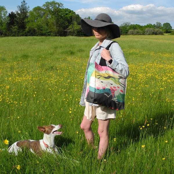 A Zoomies tote bag shown in use as a shoulder bag by a model and her whippet